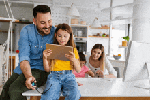 a family is sitting at a table with a man holding a tablet