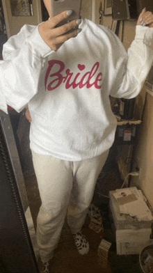 a woman taking a picture of herself in a mirror wearing a white bride sweatshirt