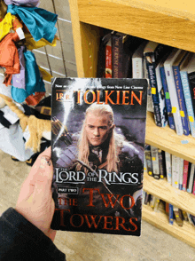 a person holding a copy of the lord of the rings part two the two towers