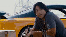 a man sits in front of a yellow sports car holding a bottle of beer