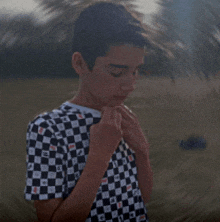 a young boy wearing a black and white checkered shirt is standing in a field