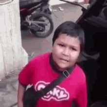 a young boy wearing a red shirt with the word carl on it is standing next to a motorcycle .