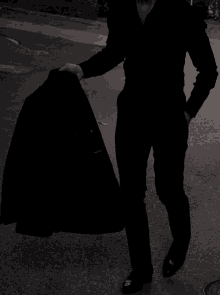 a man in a black suit is standing on the street holding a black jacket .