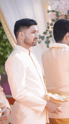 a man in a white suit stands next to another man in a tan suit