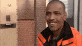 a man in an orange jacket is smiling in front of a brick building with a sign on it that says ' welcome '