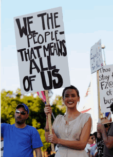 woman holding a sign that says we the people that means all of us