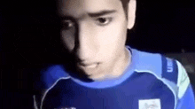 a young man in a blue shirt is standing in the dark .