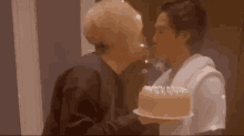 a man is kissing another man on the cheek while holding a birthday cake .