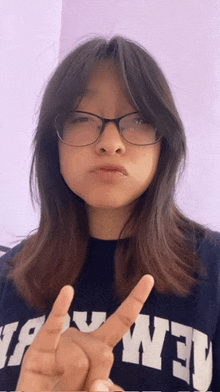 a girl wearing glasses and a shirt that says ' new york ' on it giving a peace sign