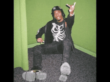 a man wearing a skeleton shirt and a hat is sitting on the floor in a room .