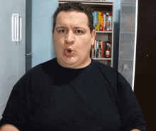 a man in a black shirt is making a funny face in front of a bookshelf with a box of coca cola on it