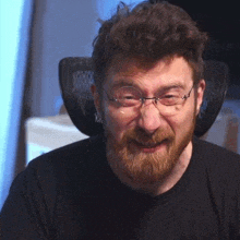 a man with a beard and glasses is sitting in a chair and smiling .