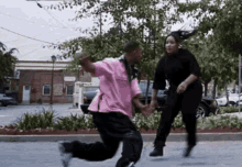 a man and a woman are dancing in a parking lot . the woman is wearing a pink shirt .