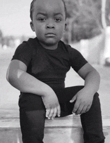 a black and white photo of a little boy sitting on a ledge