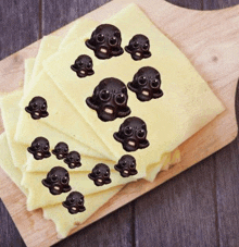 a wooden cutting board topped with a stack of cheese slices with chocolate skulls on them .