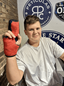 a boy wearing a white shirt holds up a red bandaged hand in front of a pet colas company sign