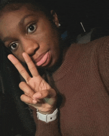 a young girl wearing a brown sweater and a white watch is making a peace sign