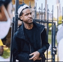 a man wearing a black jacket and a white headband is standing in front of a fence .