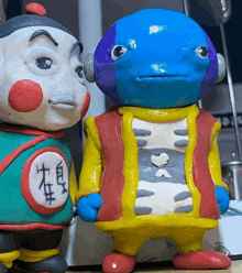 two clay figures with one wearing a green shirt with chinese writing on it