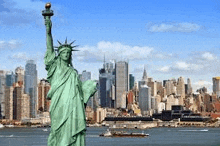 the statue of liberty is standing in front of a city skyline in new york city .