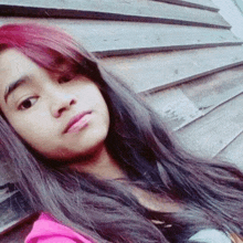 a young girl with long black and red hair is taking a selfie in front of a wooden wall .