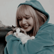 a woman in a blue hoodie is holding a cat in her arms and smiling .