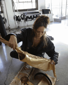 a woman in a black jacket is kneeling down and holding a piece of gold