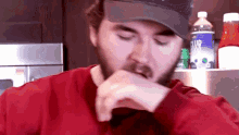 a man with a beard wearing a hat and a red shirt eating