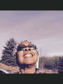 a woman wearing sunglasses and a leopard print head scarf smiles at the sun