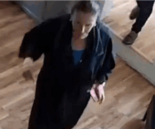 a woman in a black robe is walking down a wooden floor .