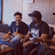 a group of men are sitting on a couch laughing while one of them is playing a guitar .