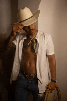 a shirtless man wearing a cowboy hat holds a rope