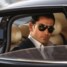 a man in a suit and tie is sitting in a car with sunglasses on .