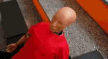 a bald mannequin wearing a red shirt is standing on a concrete floor