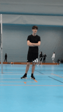 a young man stands with his arms crossed on a blue court