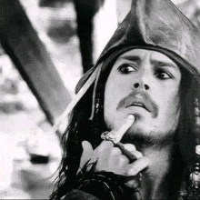 a black and white photo of a man in a pirate hat holding his finger to his chin .