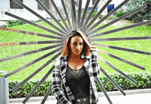 a woman in a plaid jacket stands in front of a large metal sculpture