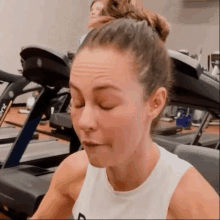 a woman is sitting on a treadmill in a gym with her eyes closed