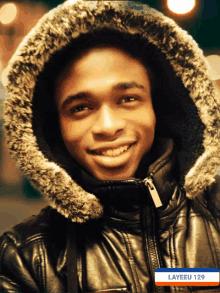 a young man wearing a fur hooded jacket with the name layeeu 129 on the bottom