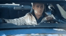 a man is driving a blue car with his hands on the steering wheel .