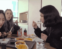 three women are sitting at a table eating food with a carton of milk in front of them with korean writing on it