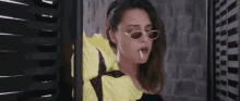 a woman wearing sunglasses and a yellow jacket is smoking a cigarette in a room .