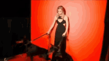 a woman in a black dress is holding a black dog on a leash