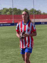 a woman in a red and white striped shirt with the word baxi on the shorts is holding a trophy