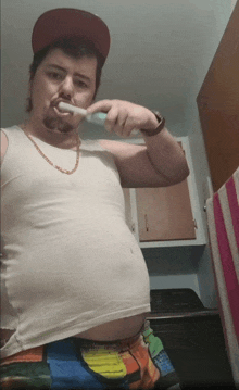 a man brushing his teeth in a bathroom wearing a hat and a tank top