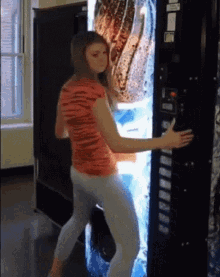 a woman is standing in front of a vending machine with a picture of a bottle of soda on it .