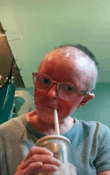 a woman with glasses and a red face drinks through a straw