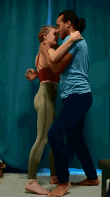 a man in a blue shirt is hugging a woman in green leggings