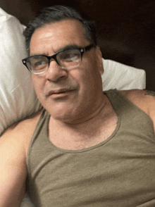 a man with glasses and a tank top is laying on a bed