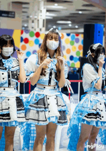 three girls wearing face masks and blue and white dresses are standing in front of a colorful polka dot wall ..